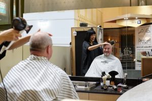 Hairdresser and client sitting in chair getting his hair cut blow waved.