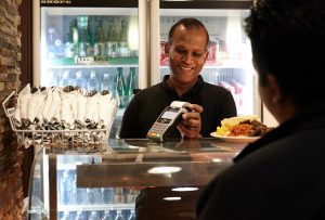 A small business owner taking a transaction using EFT over the counter at his food business shop.