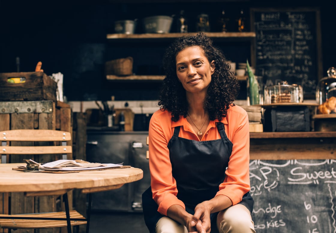 A small business owner sitting in front of their cafe with a relieved smile.